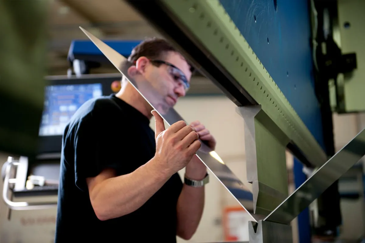 Mechaniker, der eine Schutzbrille trägt und ein eingespanntes Blechteil in der Biegemaschine hält